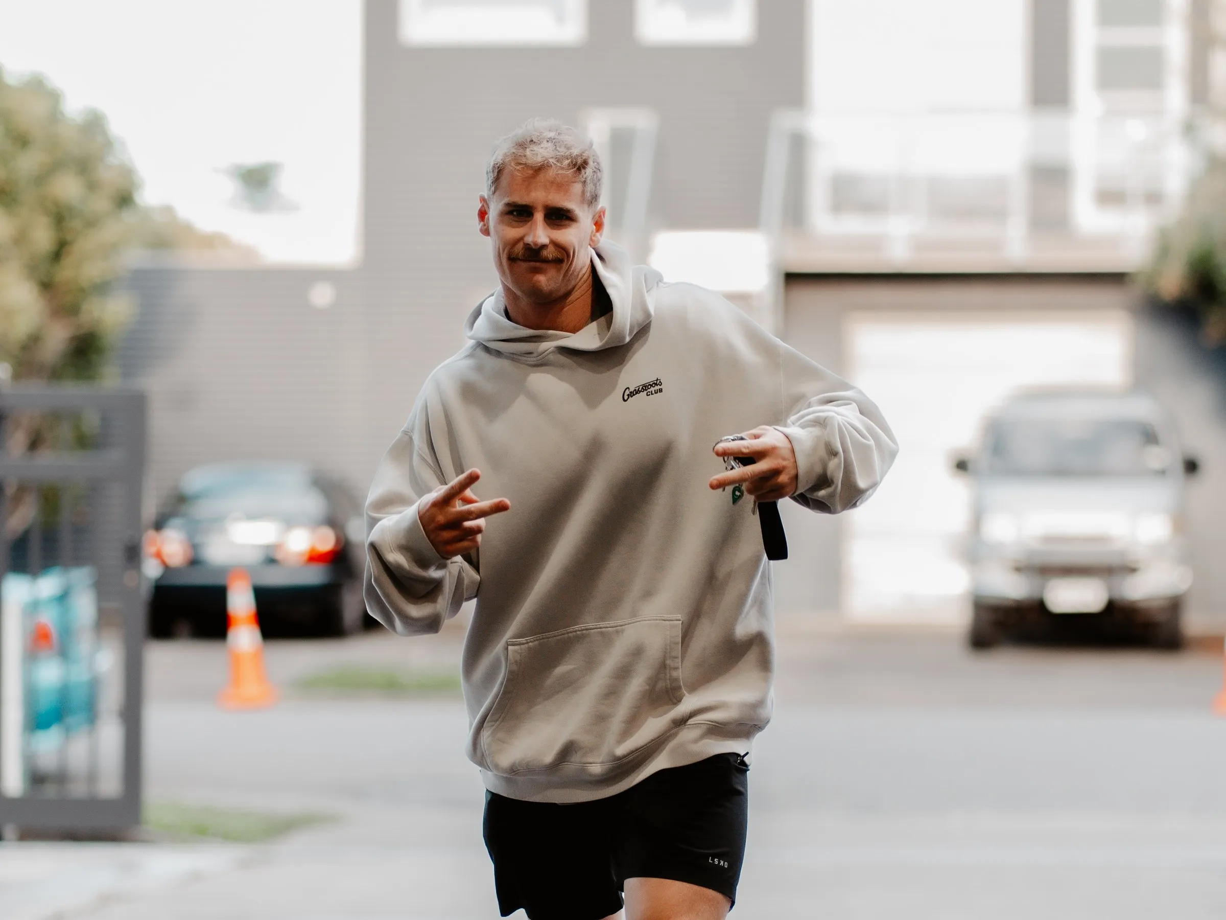 A member walking up to the gym in a Grassroots hoodie, grinning at the camera.