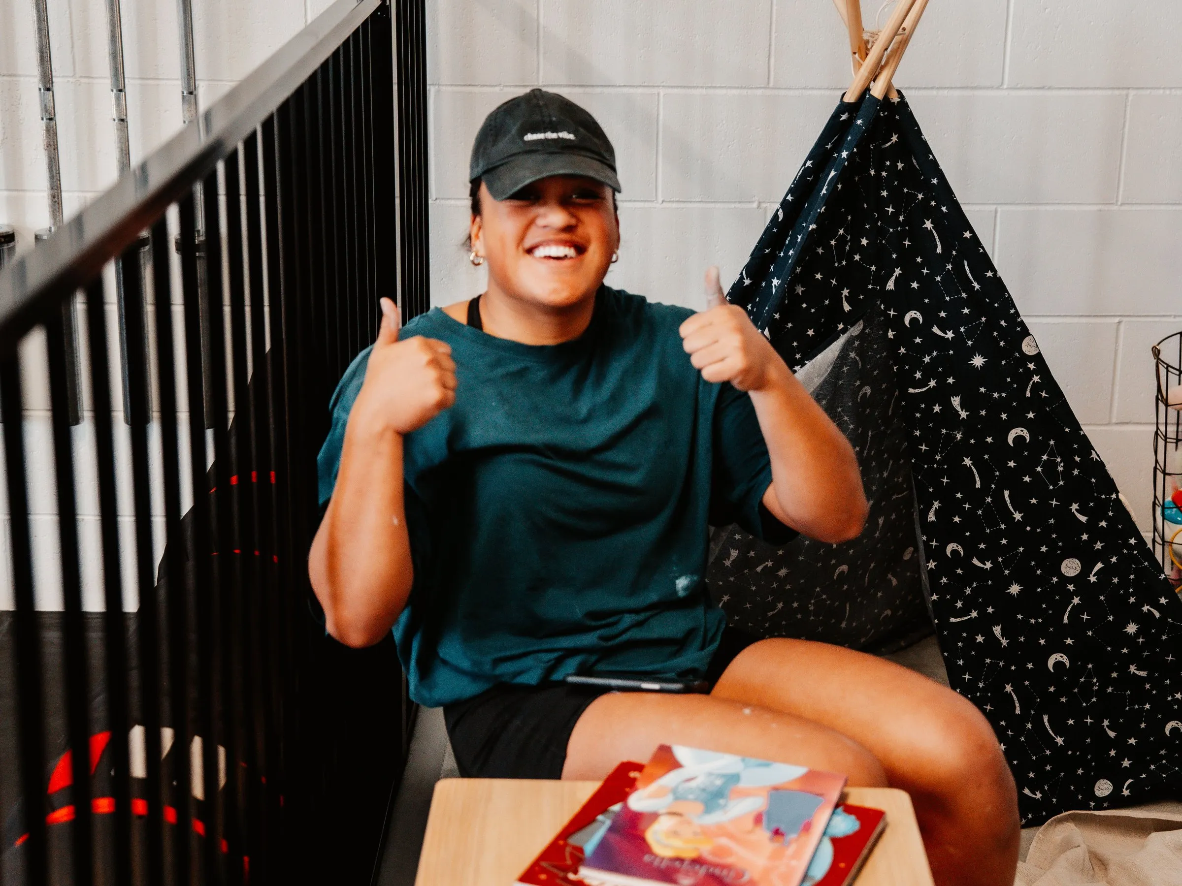 A coach sitting in the kids’ corner giving two thumbs up, teepee and picture books beside her.