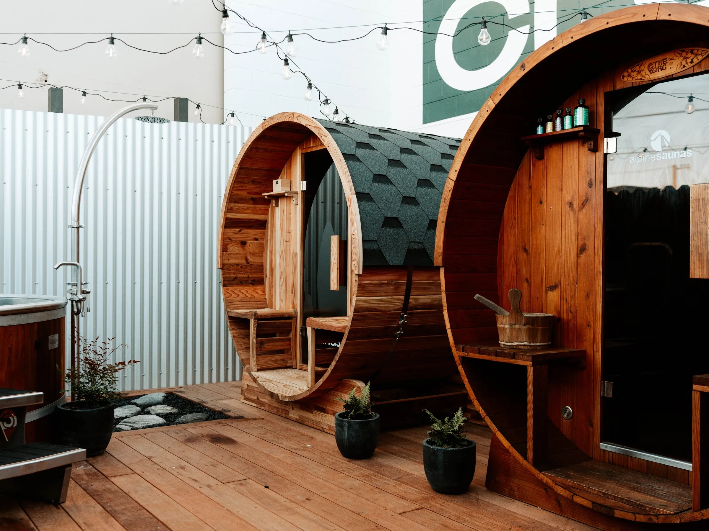 The full recovery space — ice bath and two barrel saunas under festoon lights.