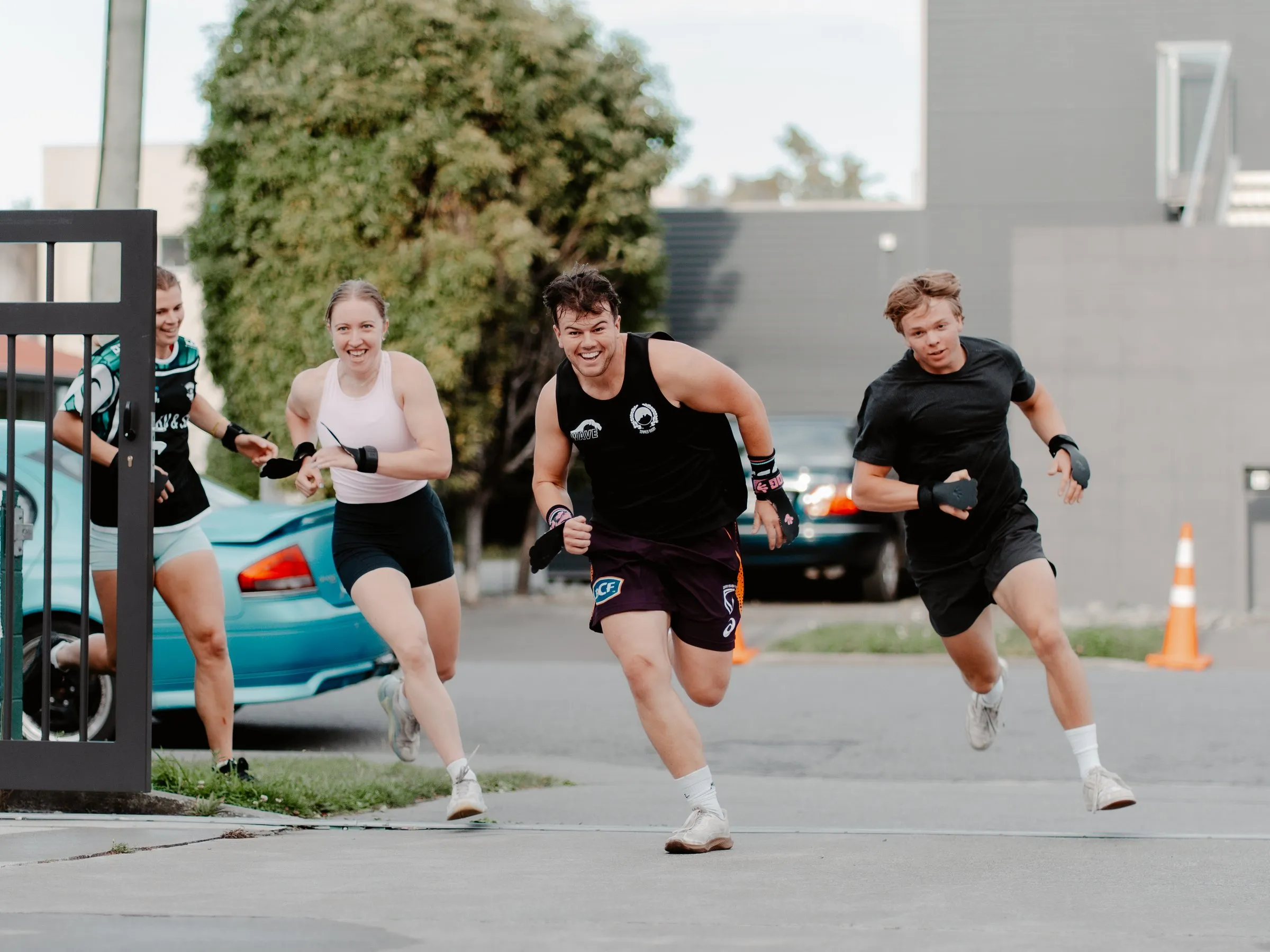 Four members sprinting up the driveway outside the gym, laughing as they race.